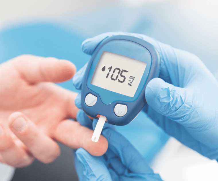 Blue-gloved hands hold a blood glucose meter